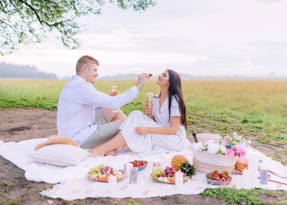 Romantic couple enjoying picnic on blanket for outdoor Valentine's Day dates under flowering trees