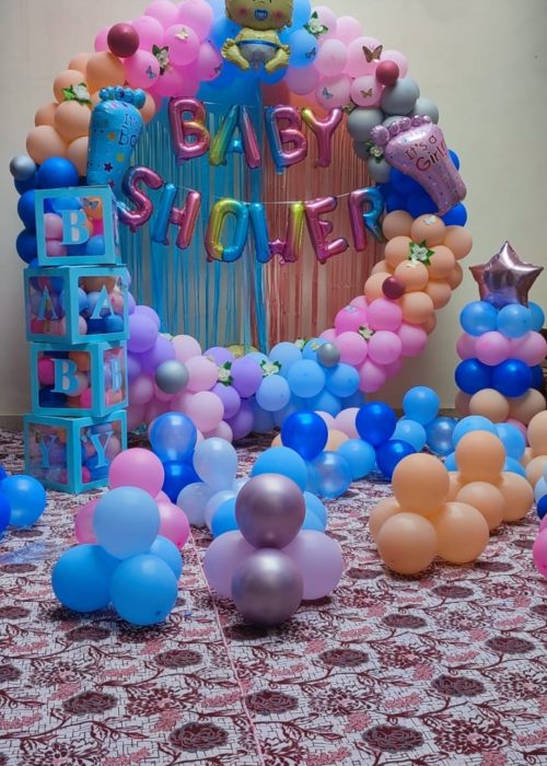 Colorful baby shower balloon ring backdrop with pastel balloons, “BABY SHOWER” letter balloons, baby-shaped balloon on top, stacked “BABY” boxes, and balloon clusters on patterned floor.